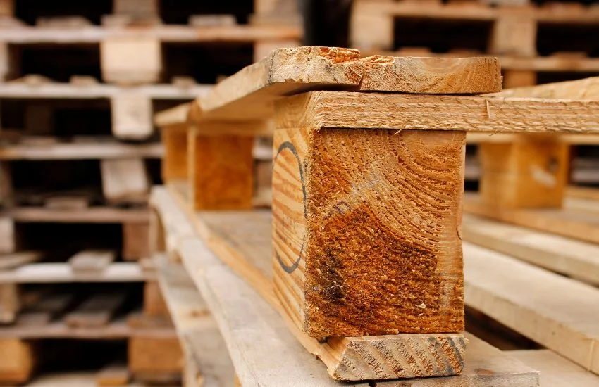 Primer plano de un palet americano fuerte de madera, con detalle de la esquina y las tablas, en un entorno de almacén industrial.
